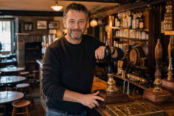 Pub bartender polishing a glass behind a traditional timber bar
